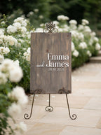 A rustic wooden wedding sign on a metal easel stand, reading 'Emma and James 28.10.
