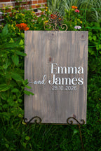 A rustic wooden wedding sign with the names 'Emma and James' and the date '28.10.